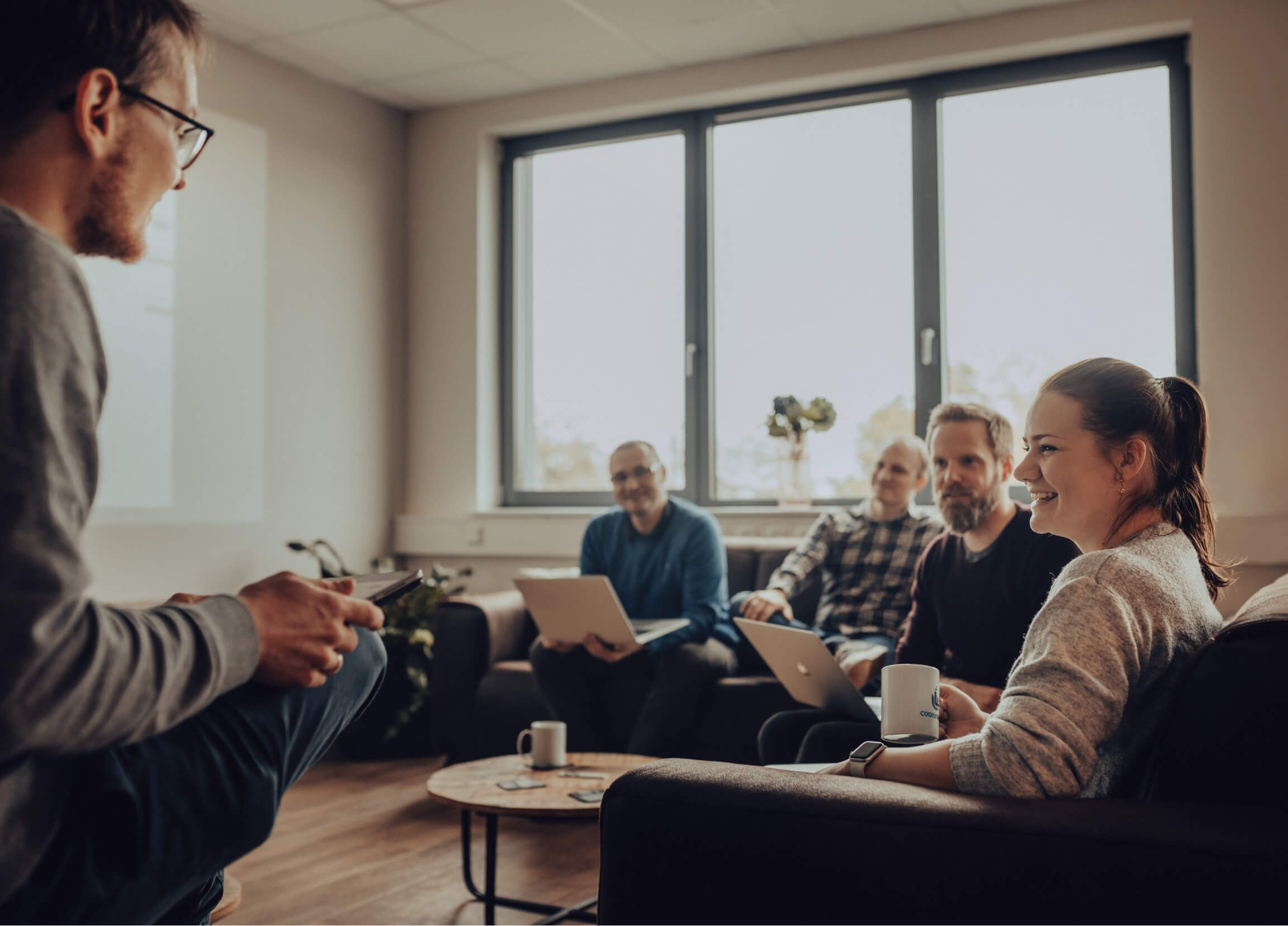 Team aus Softwareentwicklerinnen und Softwareentwicklern in einem Gespräch in einer Sitzgruppe